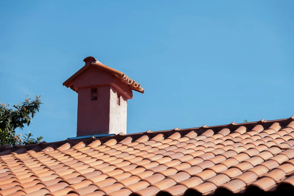 Toiture en tuiles et souche de cheminée enduite sous un ciel bleu