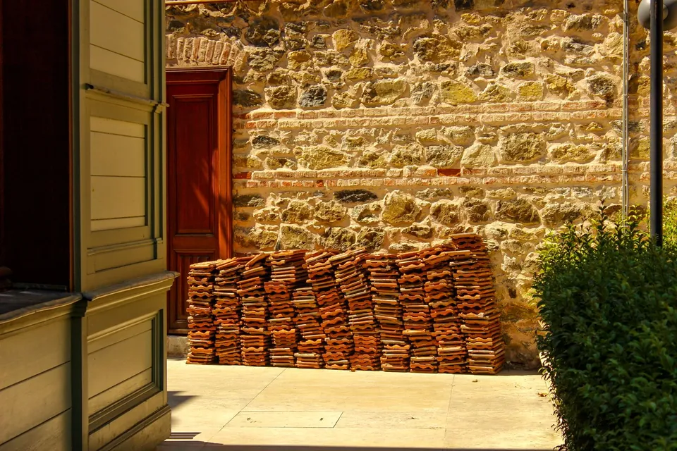 Tuiles anciennes empilées dans une cour, contre un mur en pierre